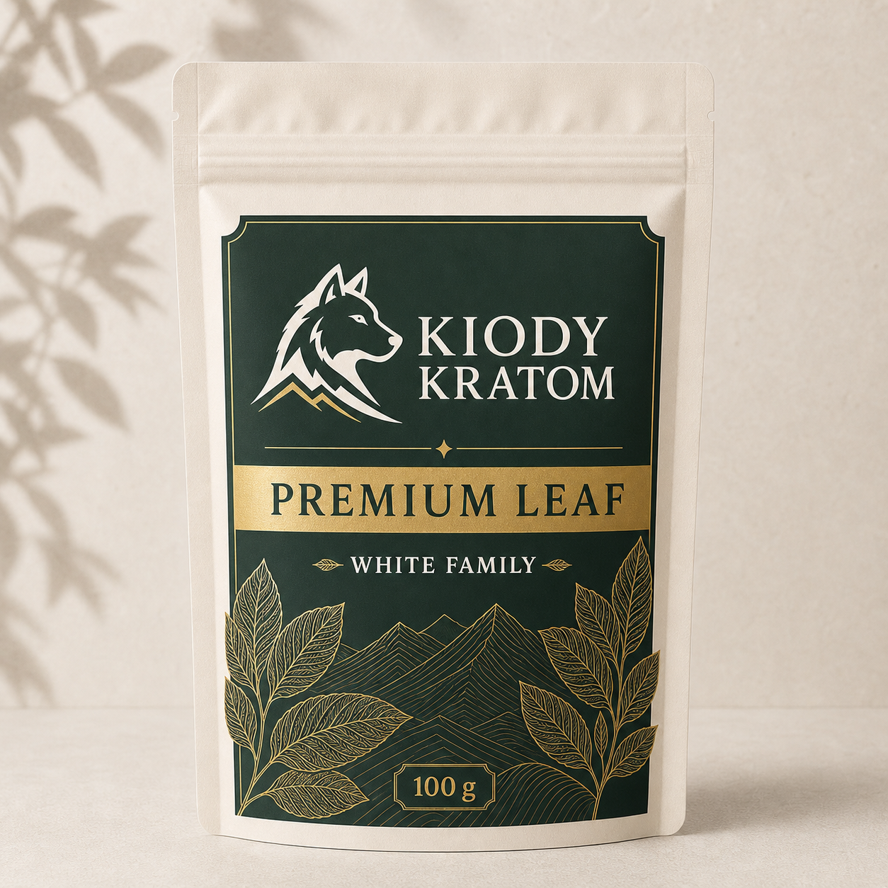 Kiody White Family Premium Leaf kratom powder in a warm ivory 100 gram pouch with gold wolf, leaves, and mountain lines