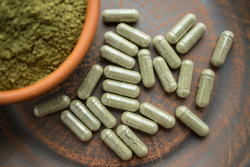 Supplement kratom green capsules and powder on brown plate.